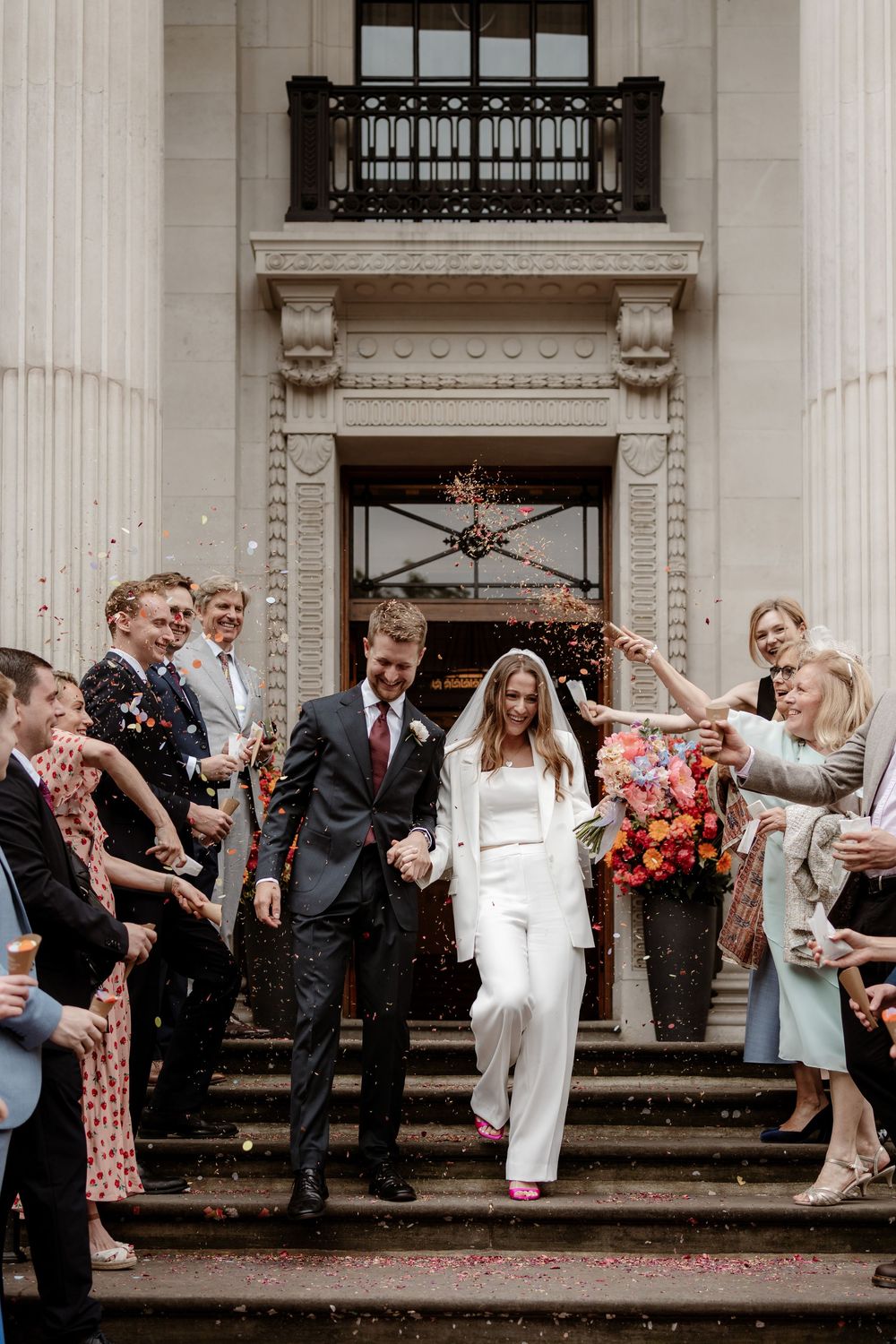 Wedding guests throw confetti on church steps as newlyweds celebrate during outdoor ceremony.