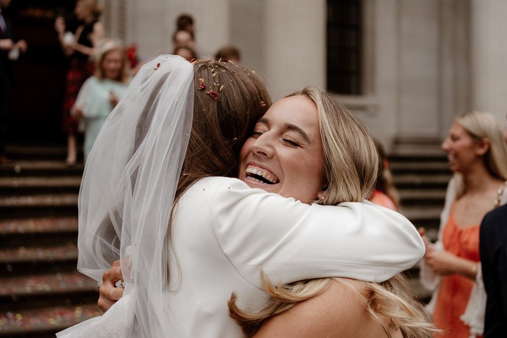 Two people share a joyful embrace on stone steps during a wedding celebration, with a white veil visible in the scene.