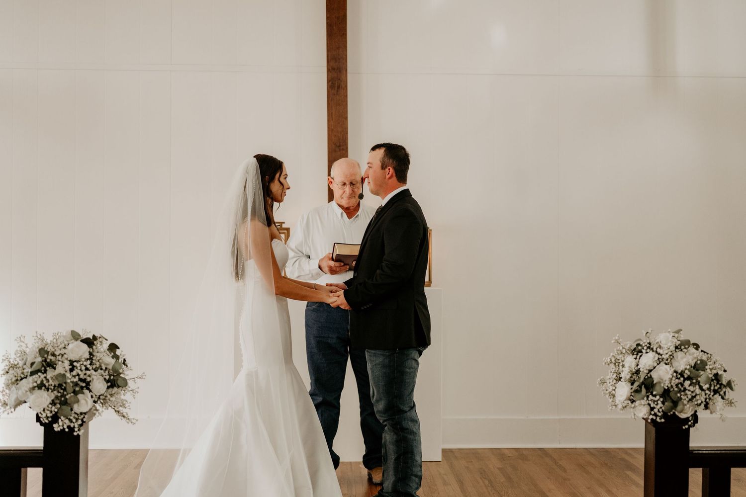 Minimalist indoor wedding ceremony with white walls and floral arrangements.