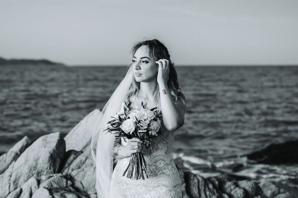 Black and white portrait of a bride holding a bouquet by the ocean.