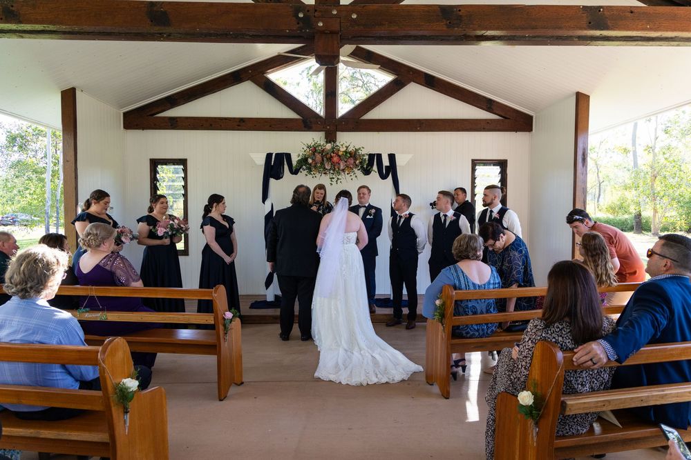Wedding ceremony taking place in rustic wooden chapel with exposed beams and wooden pews.
