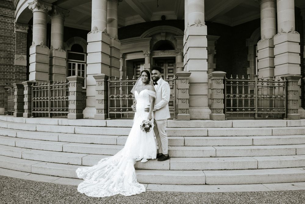 Wedding couple posing on grand stone steps with classical columns and architecture.