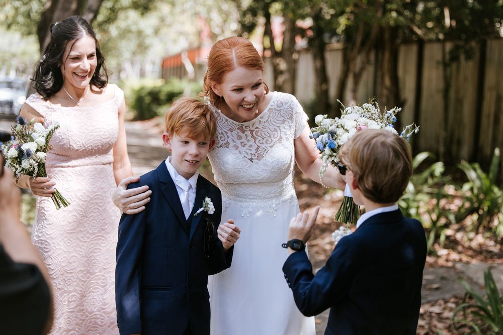 A joyful wedding scene with a bride in white lace dress sharing a moment with young ring bearers.