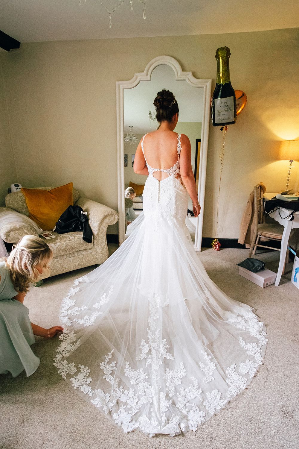 A series of photos showing a stunning white lace wedding dress with a dramatic cathedral train on display in a bedroom setting.