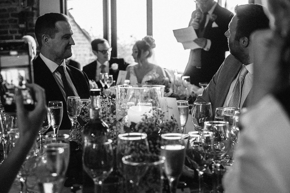 Wedding guests enjoying drinks and conversation at an elegant reception with wine glasses and table settings.