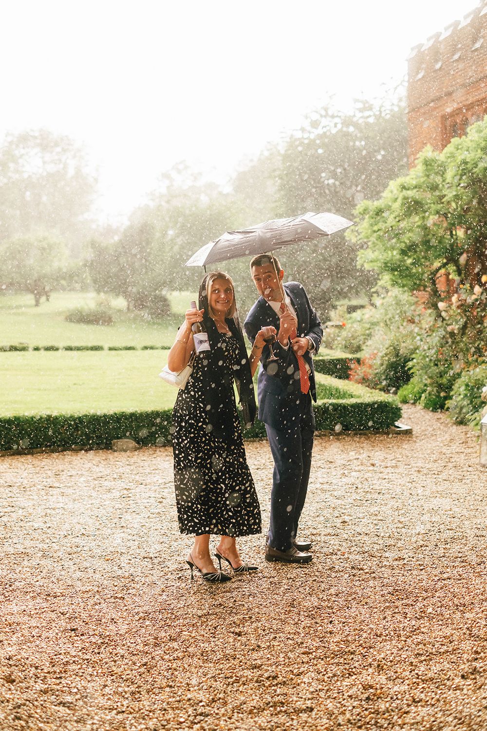 A couple shares a romantic moment under an umbrella in the rain at a garden venue.