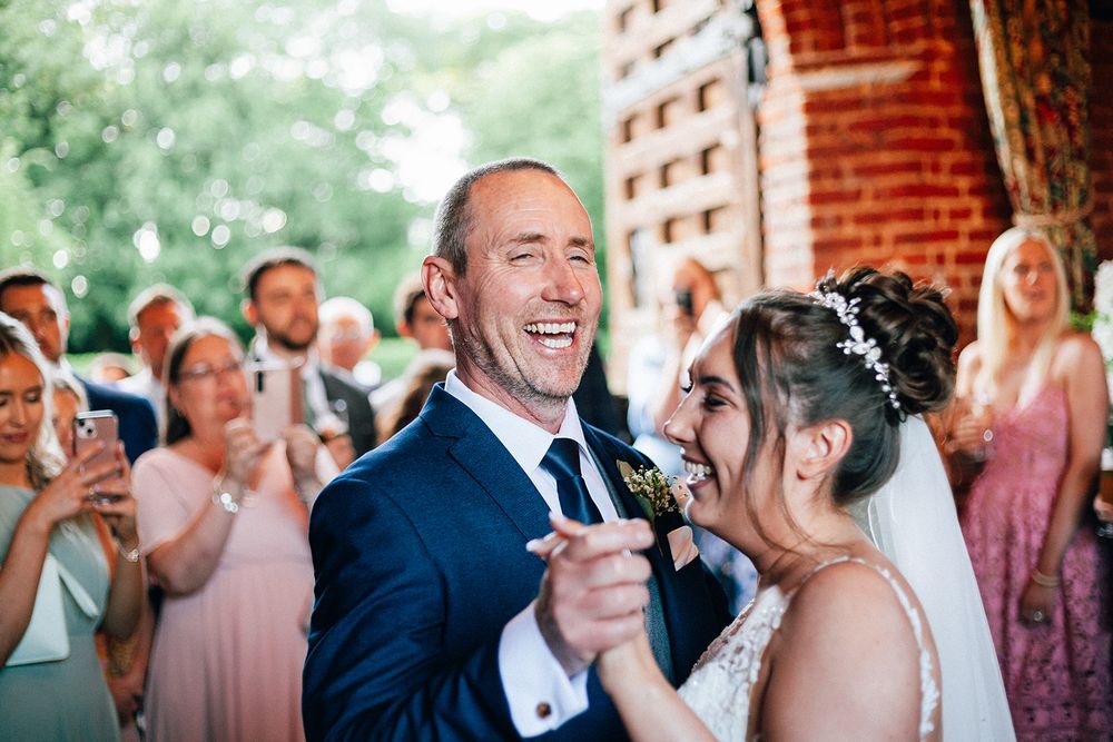 Guests share joyful laughter during an elegant outdoor wedding reception near a brick building.