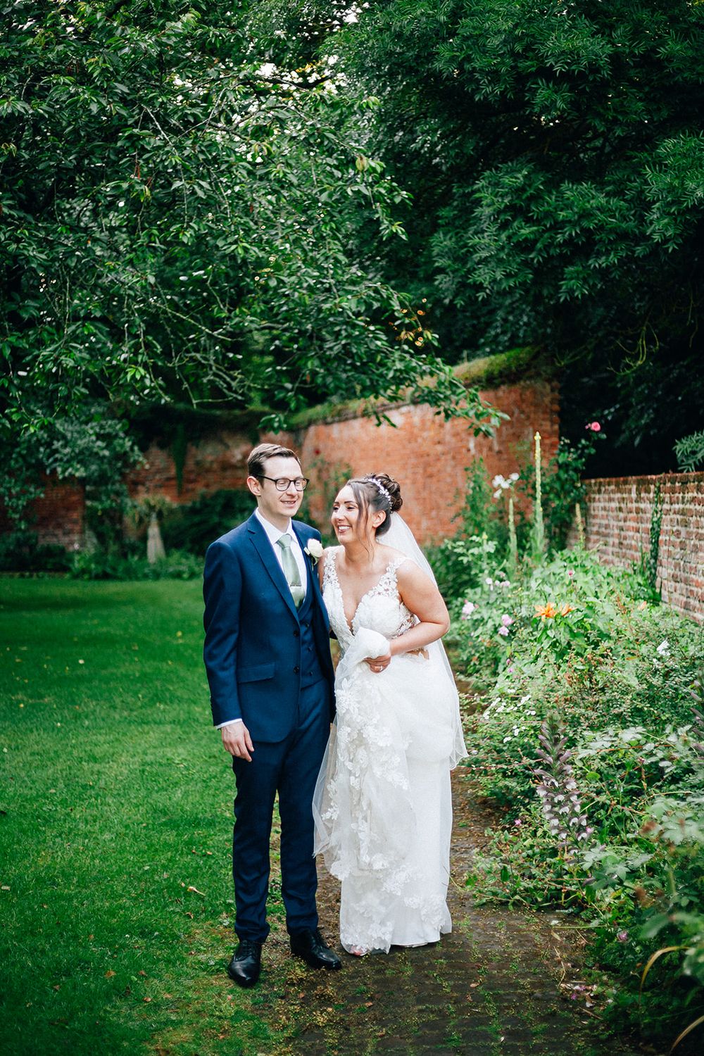 A couple shares a romantic moment in a lush garden setting with brick walls and greenery.