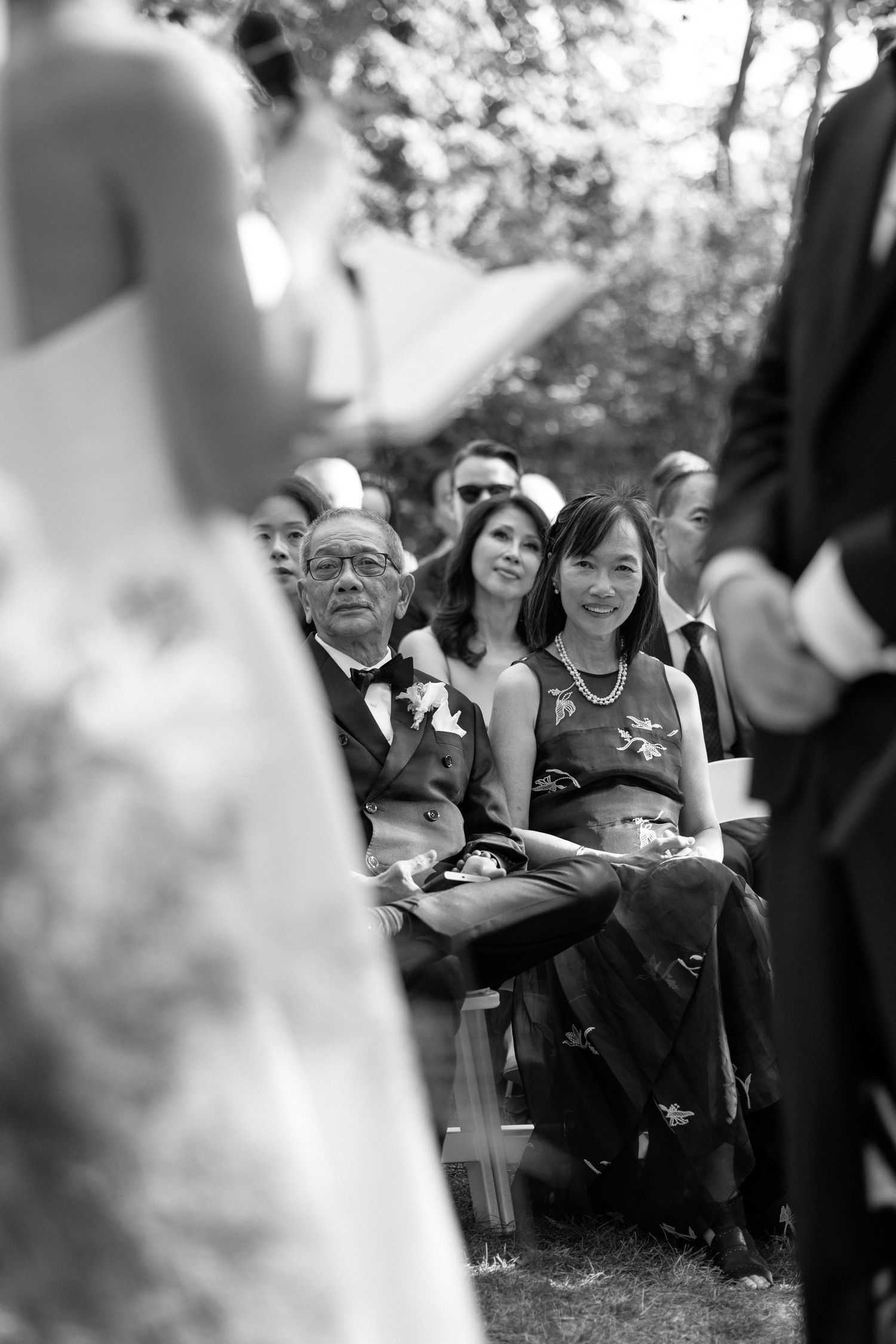 Wedding guests seated outdoors smile and watch the ceremony during a daytime celebration.