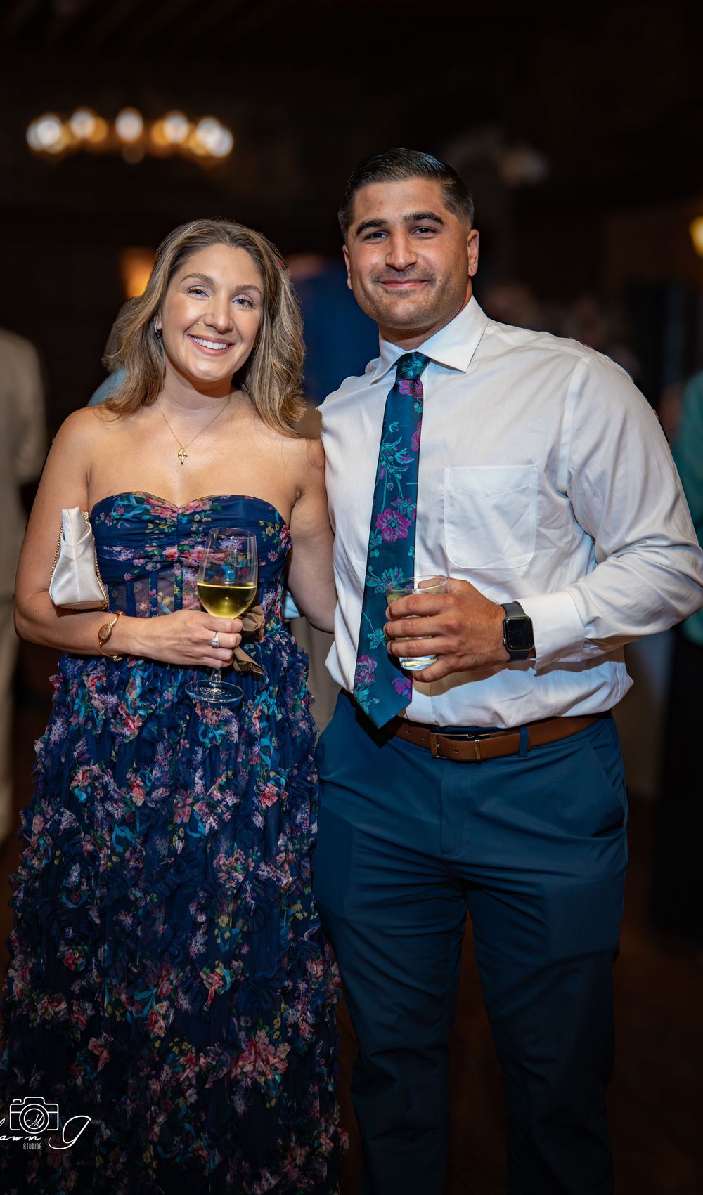 Couple dancing at wedding reception wearing navy floral dress and white shirt with blue tie.
