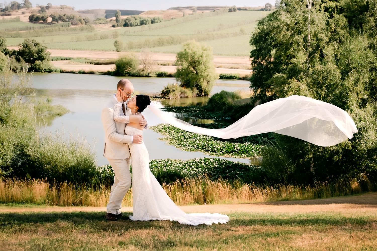 A flowing white wedding dress billows dramatically in the wind across a scenic rural landscape at sunset.