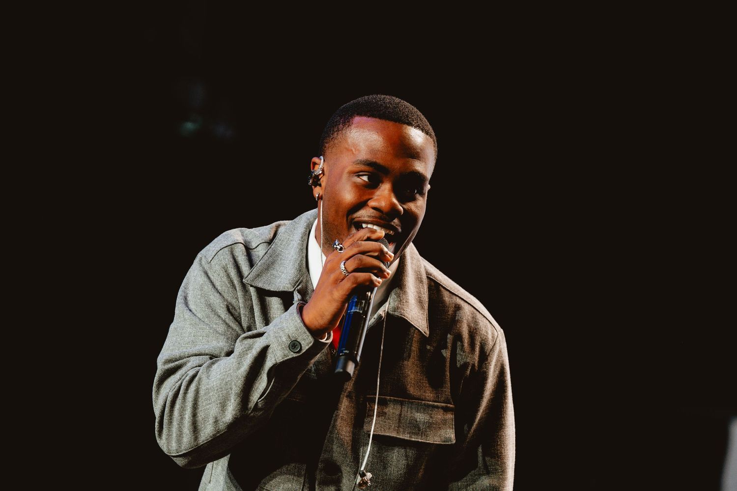A performer sings passionately into a microphone while performing on stage in dramatic lighting.