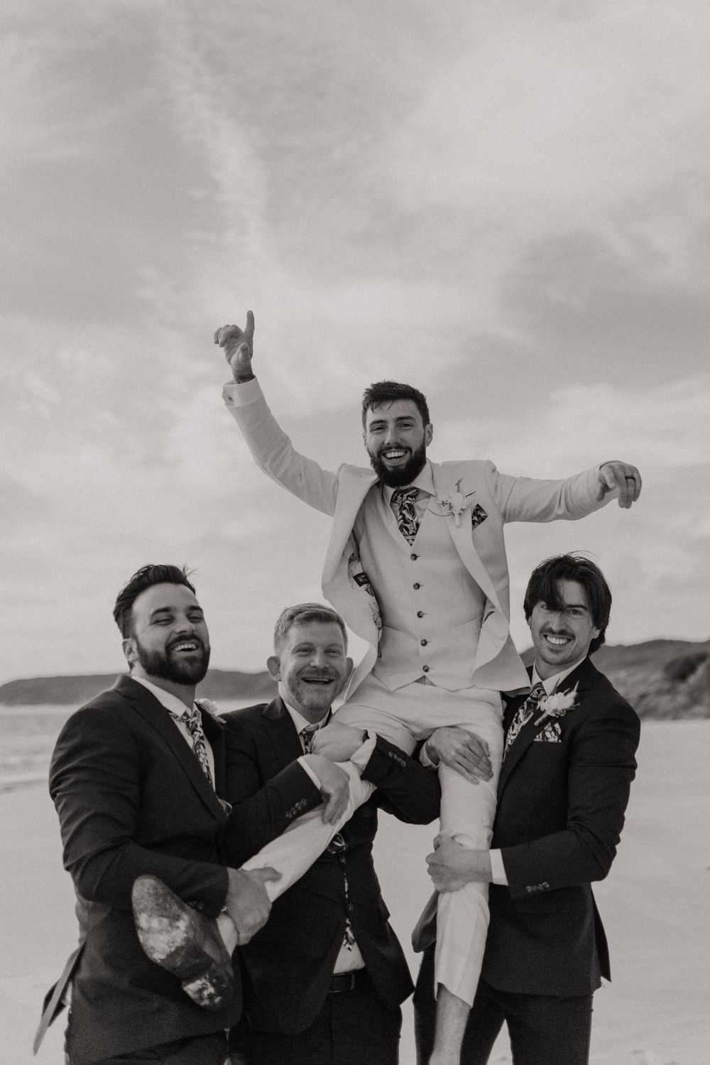 A sequence of black and white photos showing groomsmen playfully lifting and tossing someone in formal attire at an outdoor event.
