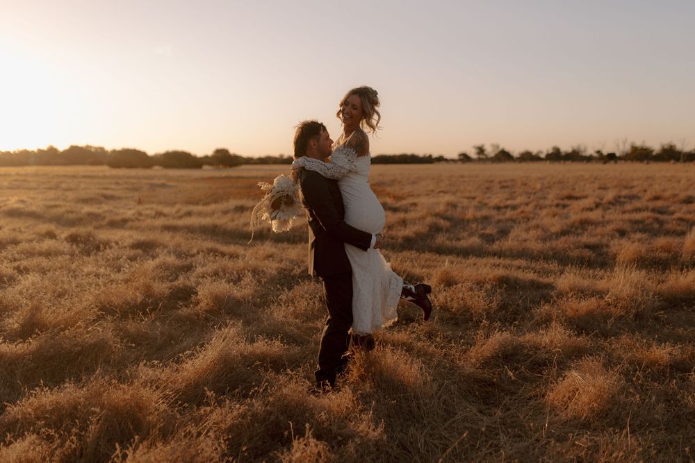 A couple embraces in a golden field at sunset, silhouetted against the warm evening sky.
