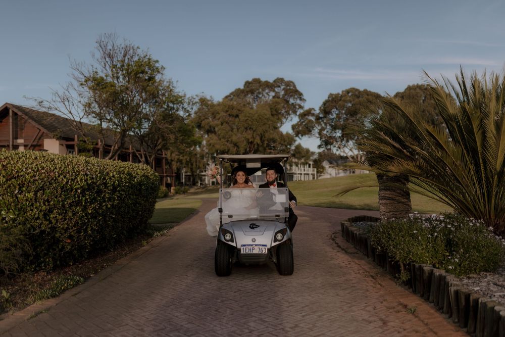 A golf cart drives along a winding path through a scenic golf course surrounded by palm trees and lush landscaping.