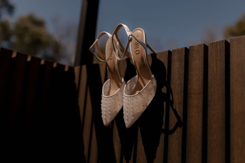 A row of elegant beige high heeled shoes displayed against a dark wooden fence background.