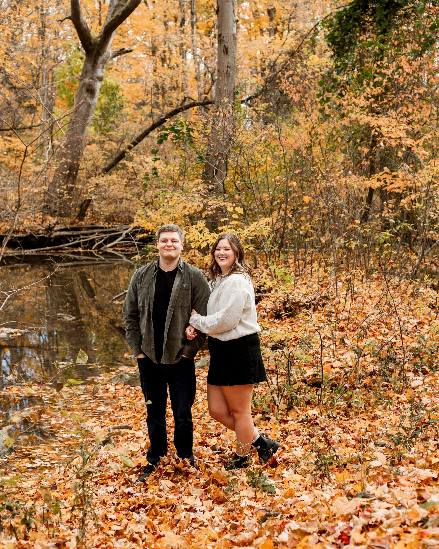 A couple shares a joyful moment together in a golden autumn forest setting during a photo session.