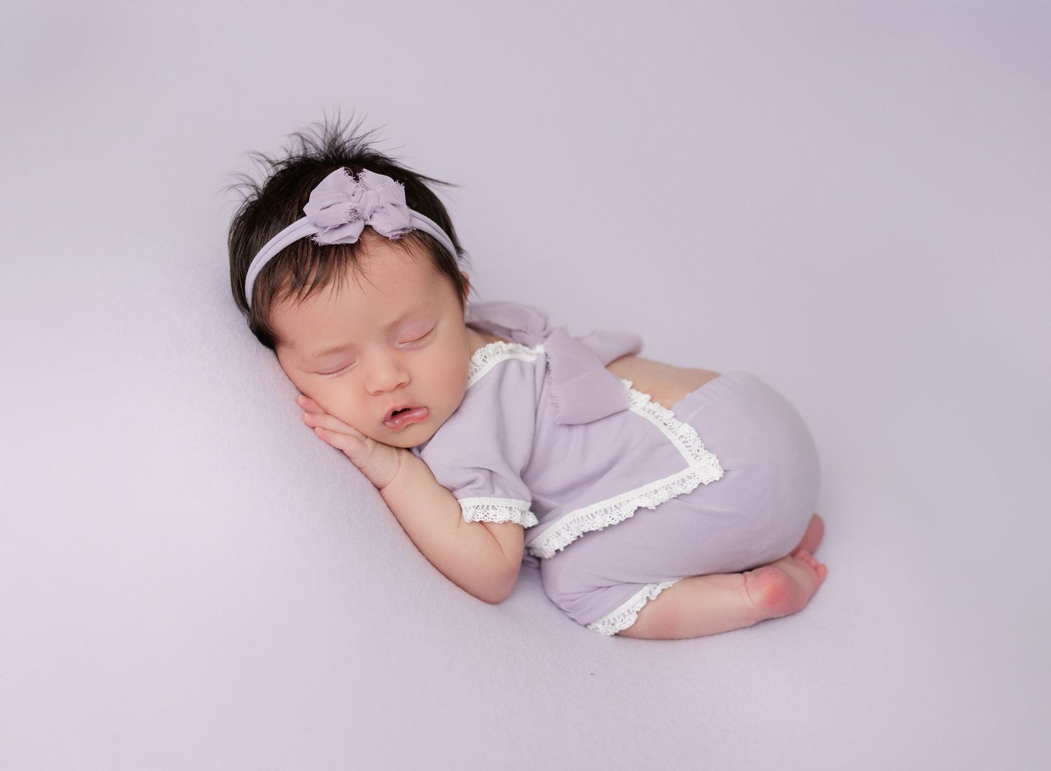 Sleeping newborn in white wrap with delicate lace headband.