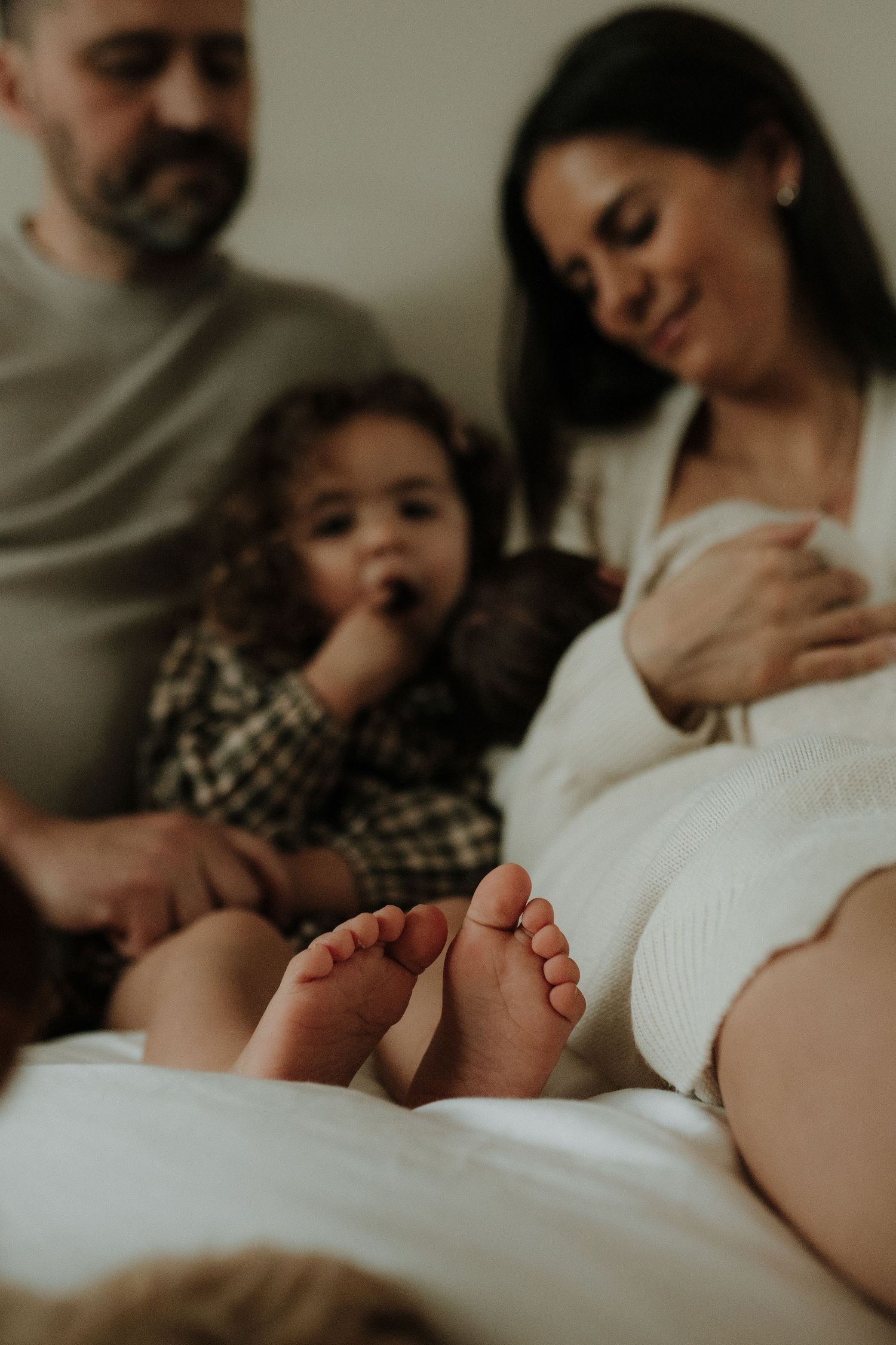 Family lying together in bed sharing intimate bonding moments in a series of warm, candid photographs.