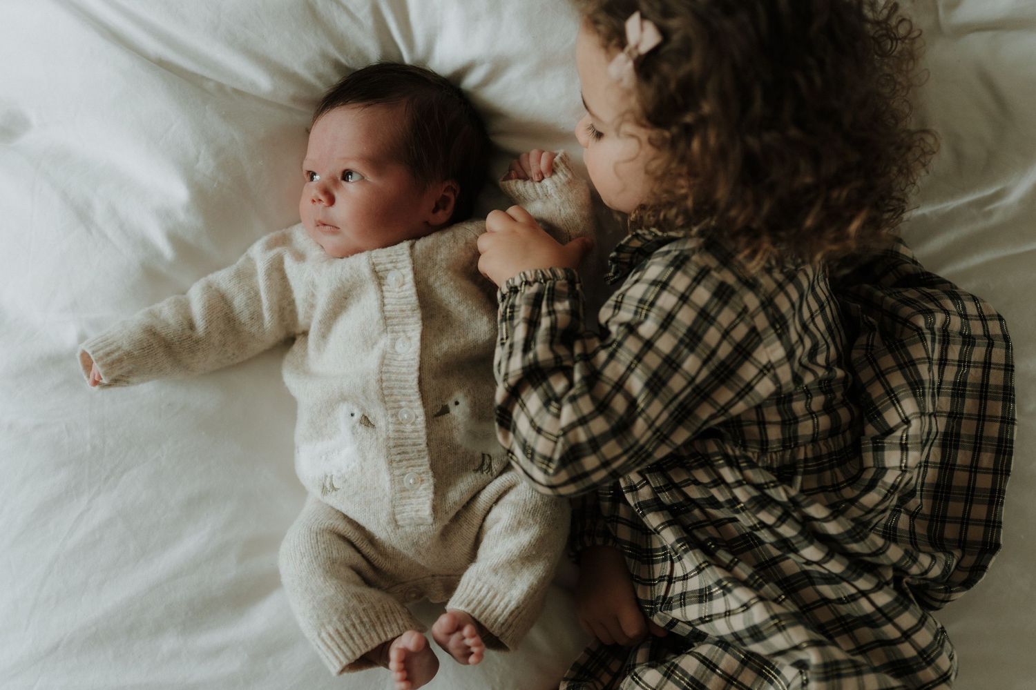 Baby sleeps peacefully on white bedding while being held in a plaid shirt-wearing embrace.