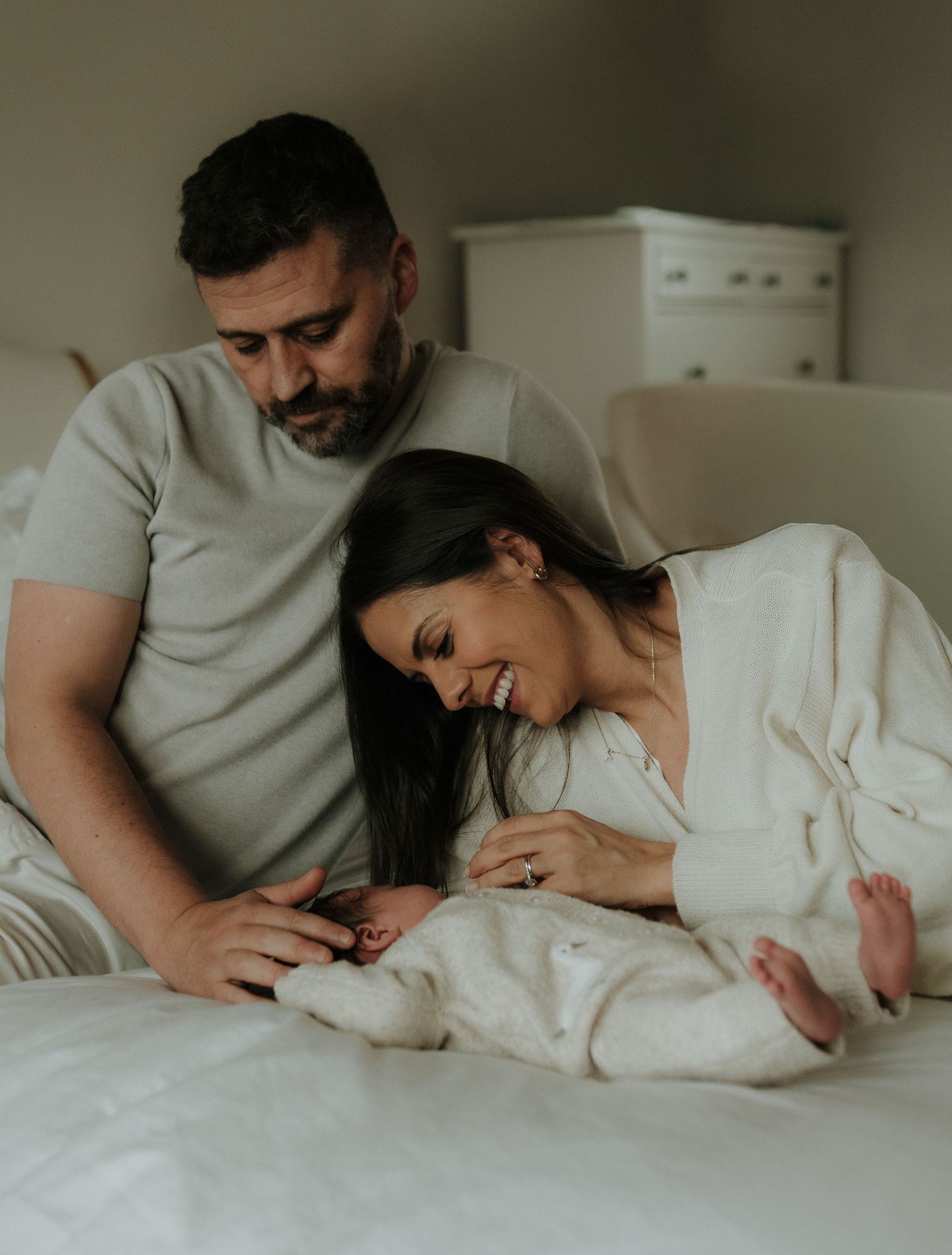A couple lying together on white bedding sharing an intimate moment in natural lighting.