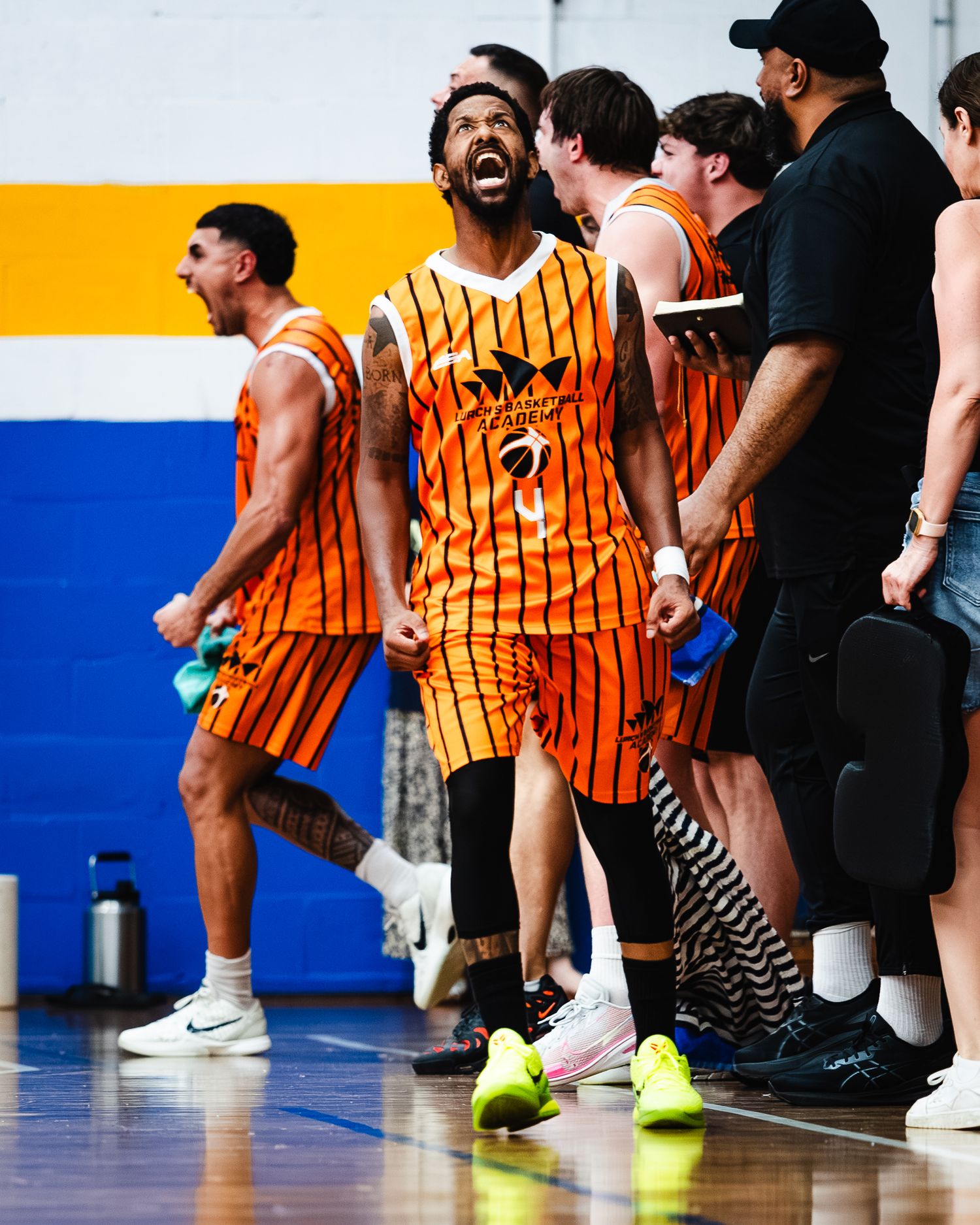 Basketball players in orange striped uniforms gather on sideline during game.