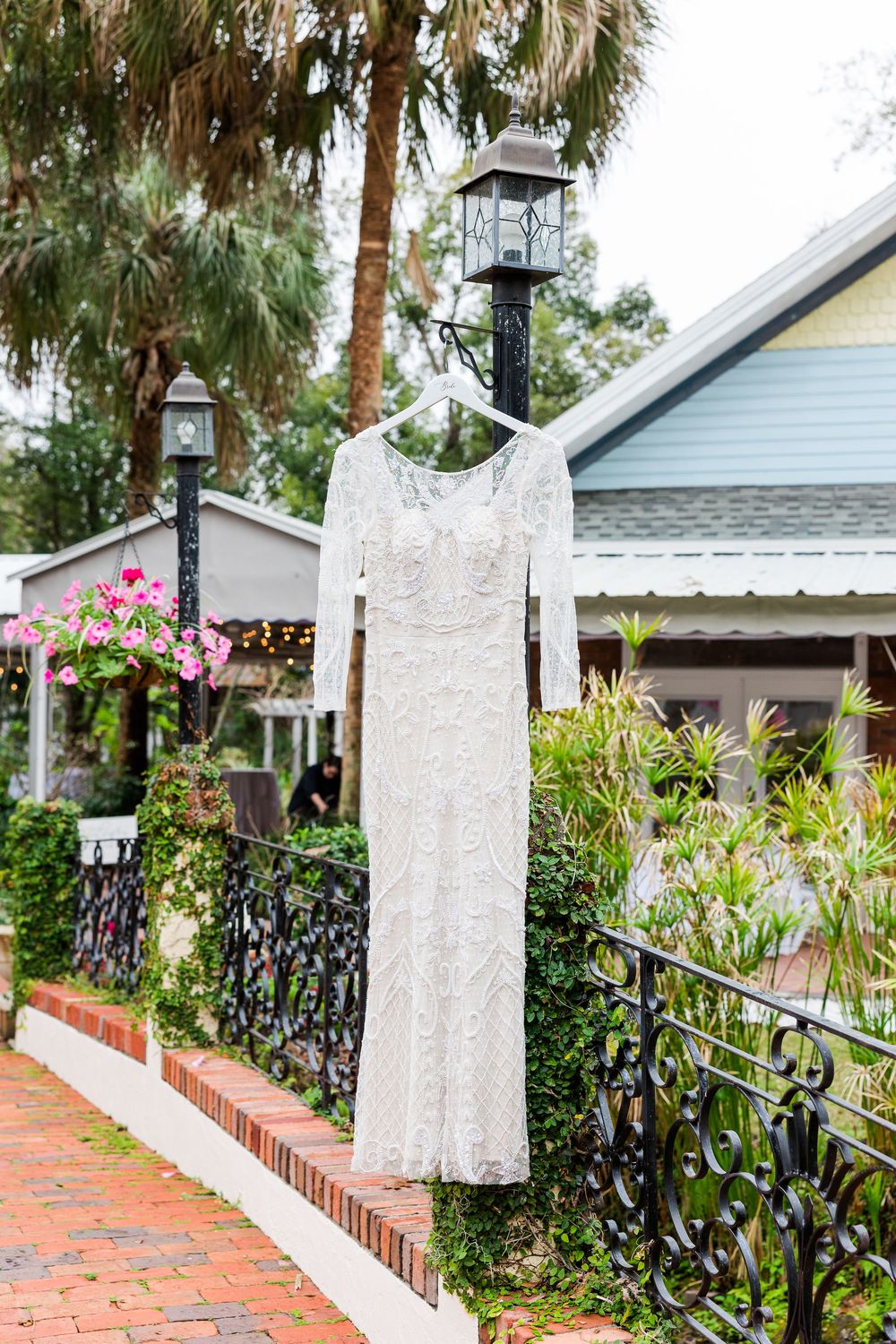 Decorative white lantern posts and brick wall with lush tropical landscaping along a garden pathway.