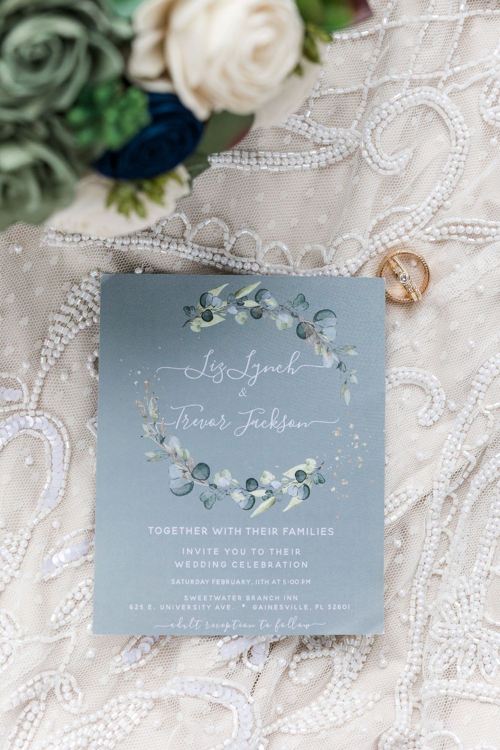 Elegant dusty blue wedding invitations with floral designs and calligraphy on white lace background.