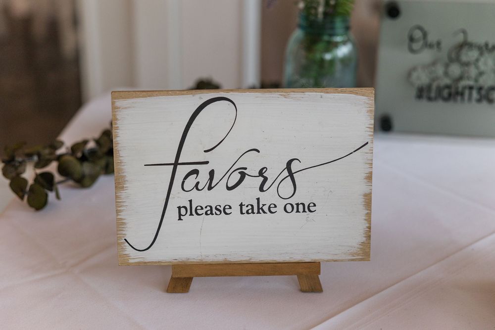 A row of wooden signs with elegant calligraphy displaying 'Please take one' text at a wedding or event.