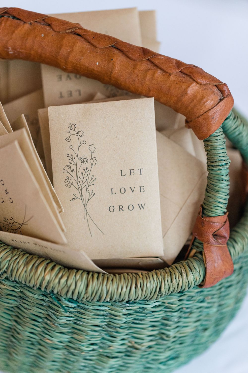 Handmade paper envelopes with delicate floral sketches and text 'LOVE' arranged in a mint green woven basket.