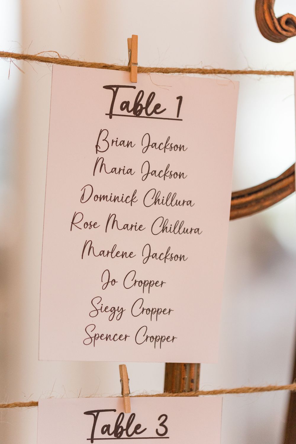 Wedding seating chart with names displayed on white cards attached to twine with wooden clothespins.