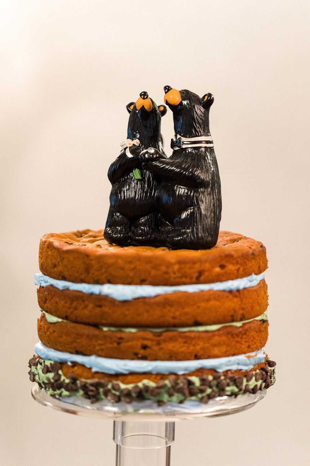 A layered chocolate cake with blue frosting and penguin decorations on top displayed on a cake stand.