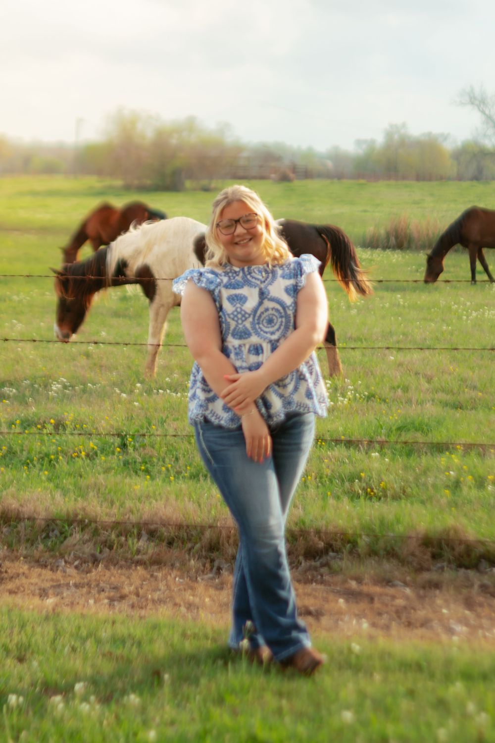 A couple embraces in a sunny field while horses graze in the background on a spring afternoon.