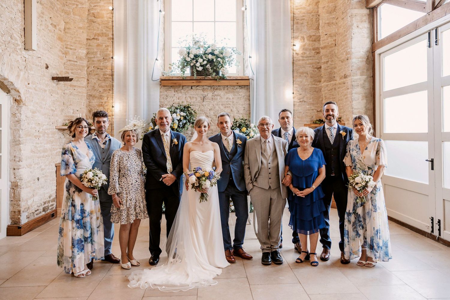 Wedding party members and guests gathered in a rustic brick venue with large windows and natural lighting.
