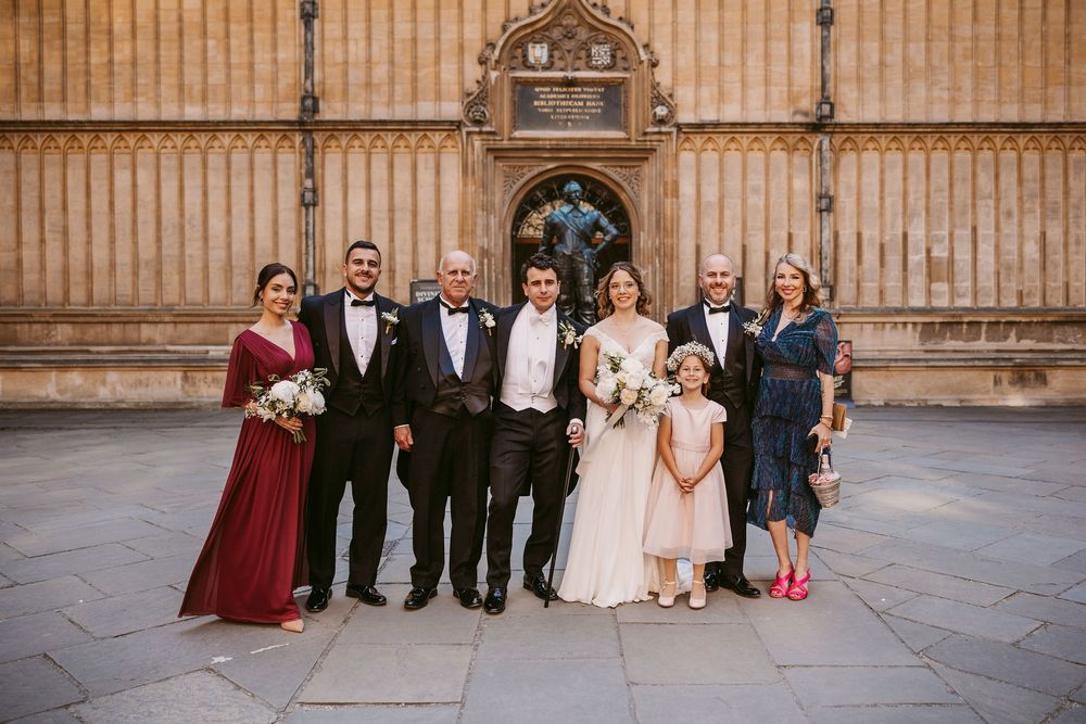 Wedding party group photos lined up against a grand stone building with gothic architectural details.