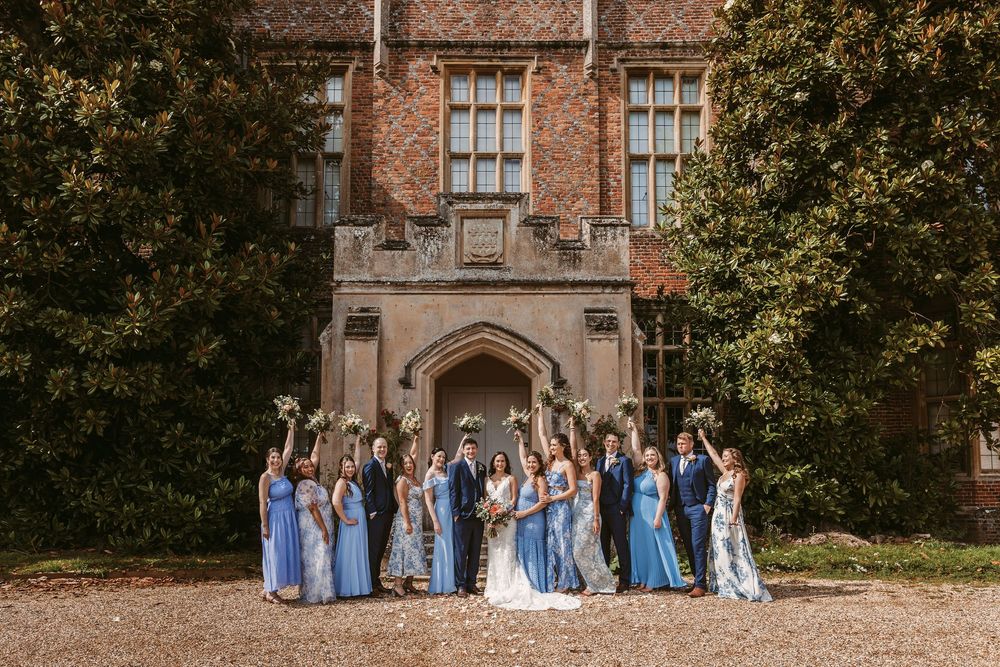 Wedding party in light blue dresses poses together on stone steps of historic brick building in autumn.