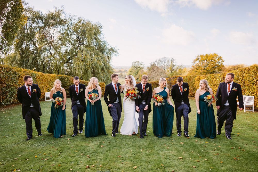 Wedding party in formal attire poses together on a grassy field during golden hour.