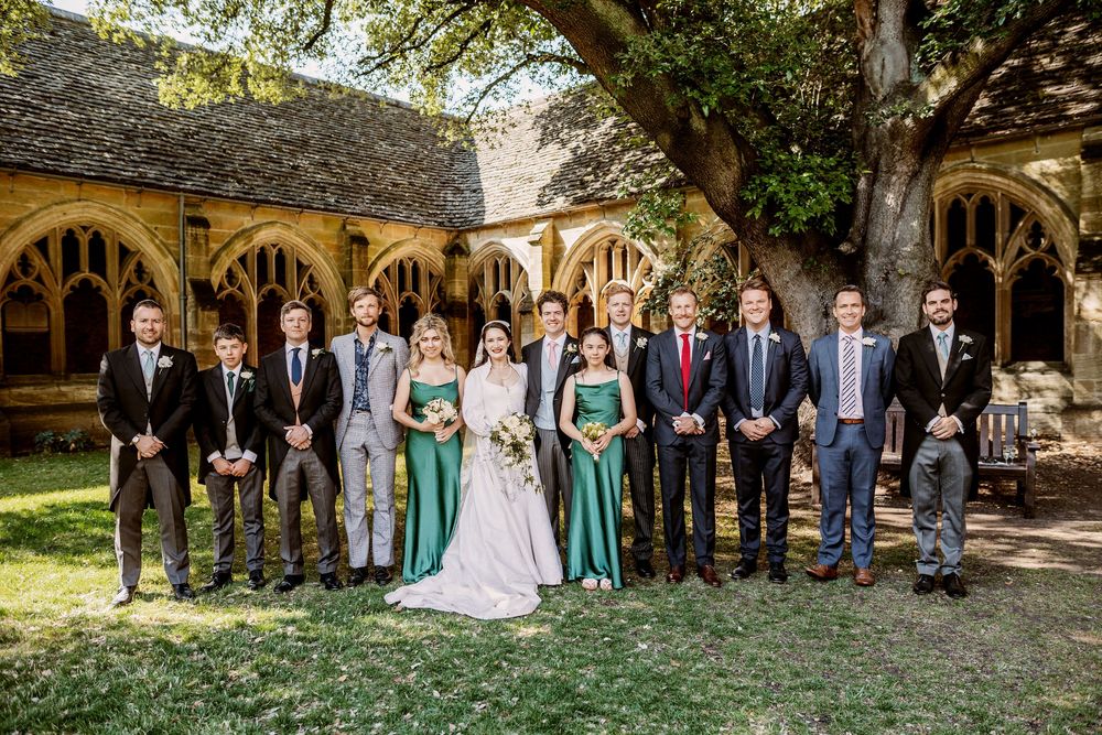 Wedding party members arranged in a line under stone archways at an elegant venue.