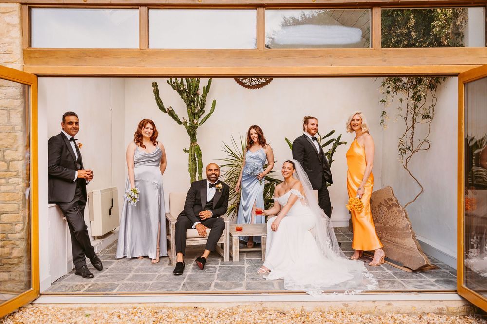 Wedding party poses in front of a stone wall backdrop in a rustic venue.