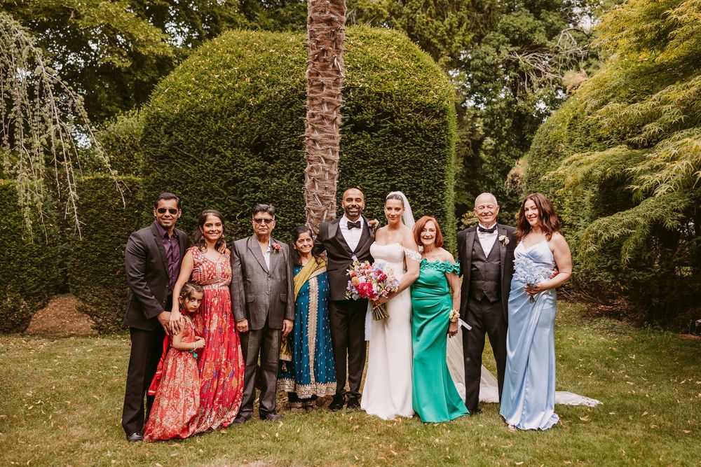 Wedding group photo with colorful attire gathered in a lush garden setting.