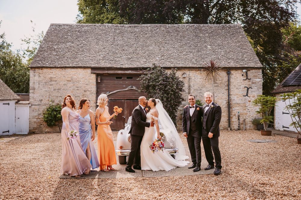 Wedding party poses for group photos in front of a rustic stone building with pink bridesmaid dresses.