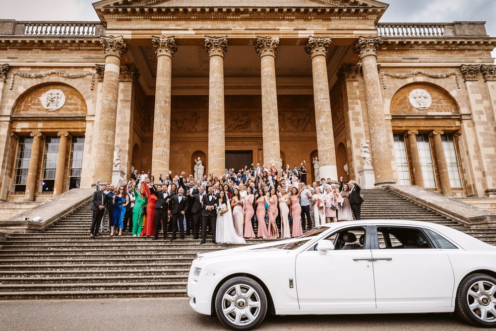 Luxury white wedding car parked in front of grand classical stone building with columns.