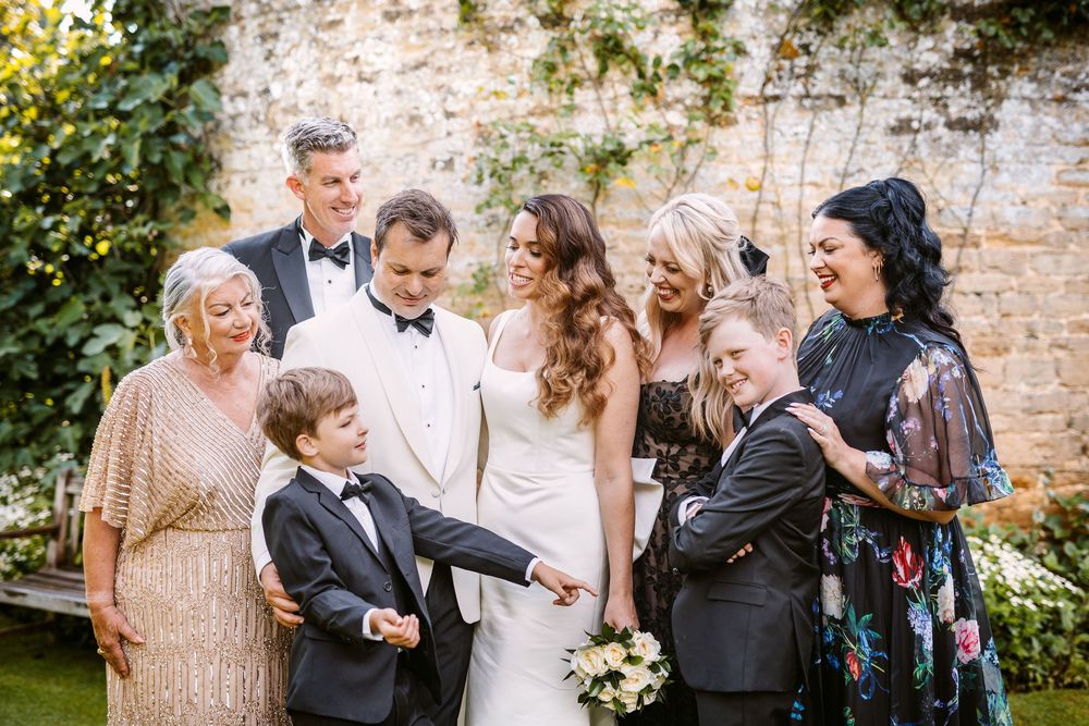 Wedding guests share candid moments of laughter and joy during an outdoor celebration by a stone wall.