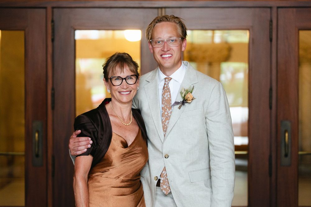 A group of people in formal attire pose together at an event in front of wooden doors.