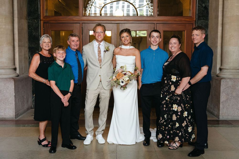 Wedding party members pose in formal attire inside an elegant venue with arched doorways.