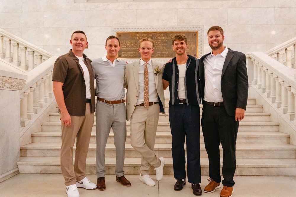Five people in formal and business casual attire stand together on white marble stairs for a group photo.