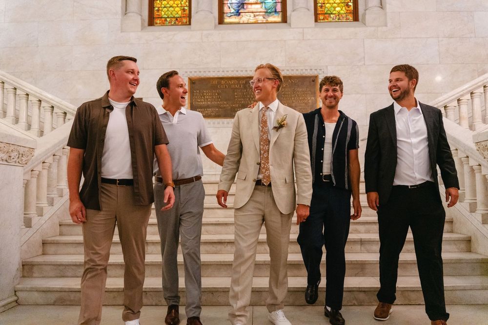 Wedding party members walk together on marble stairs in coordinated formal attire.