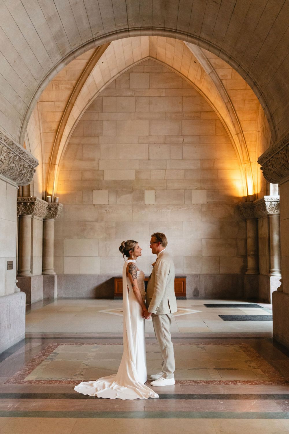 A couple shares an intimate moment under Gothic stone arches illuminated by warm lighting in a historic venue.