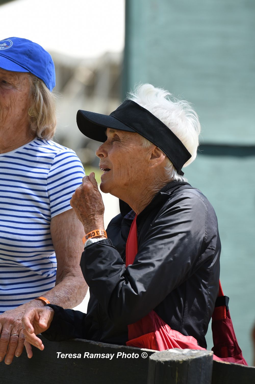 Two seniors in casual attire enjoying ice cream outdoors, one wearing a blue cap and striped shirt, the other in black.