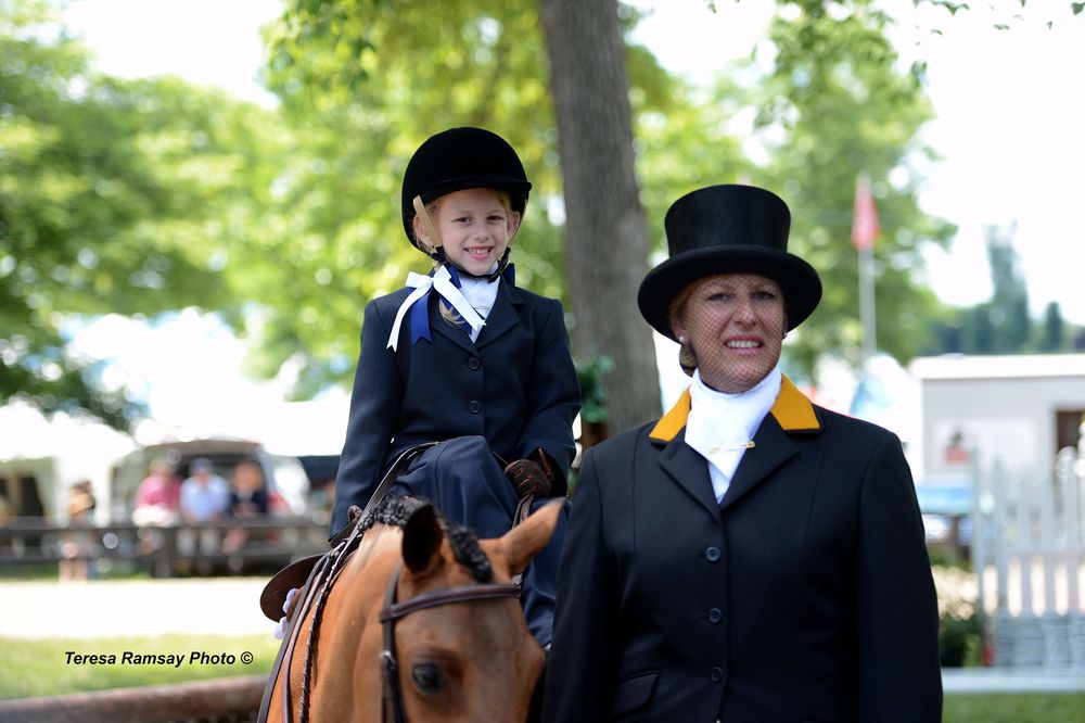 Equestrian riders in formal attire compete in a horse show event at an outdoor arena.